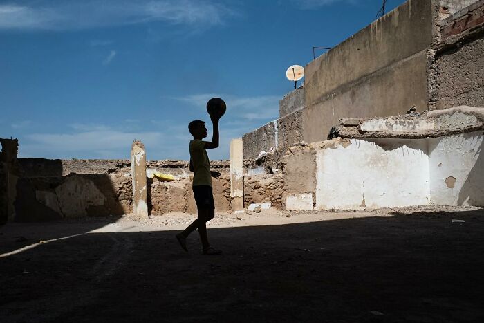 A boy with a ball in silhouette, set against an urban backdrop under a clear sky, showcasing street photography.