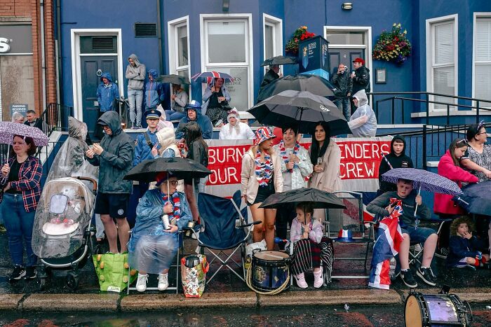 Crowd with umbrellas in a rainy street scene, featuring diverse people in a candid moment by Andrea Torrei.