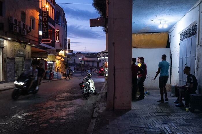 Street scene at dusk with people gathered under a lit canopy, capturing a curious eye on urban life and activity.