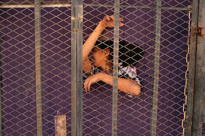 A person gazing through a fence with curiosity, captured in street photography by Andrea Torrei.
