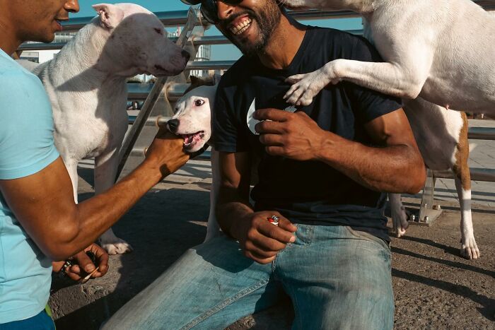 Two men smiling with three playful dogs, capturing a moment of joy in street photography.