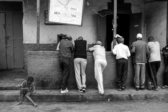 Street photo by Andrea Torrei showing a group of men leaning on a wall, with a child sitting nearby.