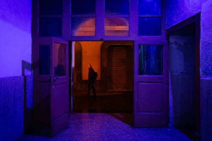 Street photo with vibrant colors showing a person walking under an archway, as captured by Andrea Torrei.