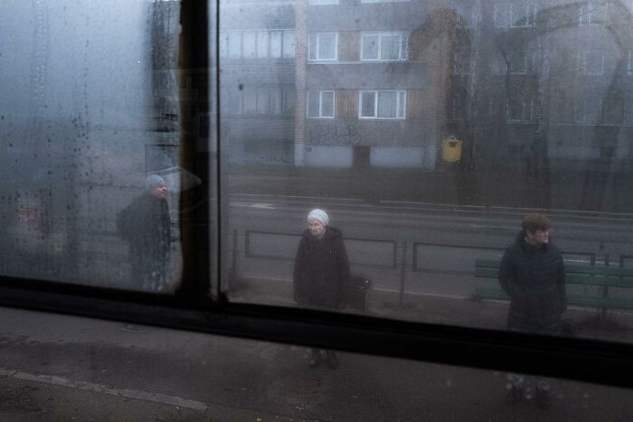 Street photo by Andrea Torrei showing people waiting by a gloomy roadside, viewed through a rain-spattered window.
