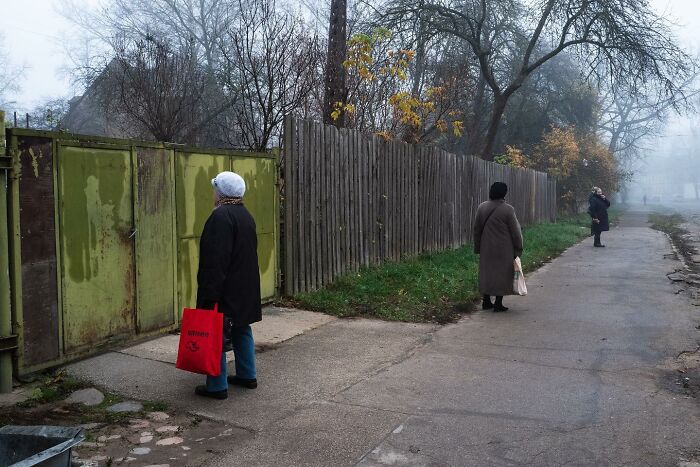 Street photography by Andrea Torrei showing people standing near a wooden fence on a foggy day.