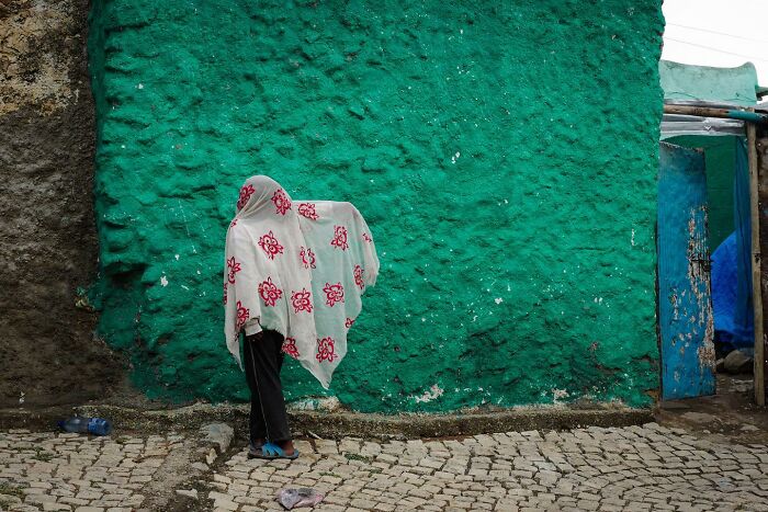 Street photo by Andrea Torrei: person wrapped in a patterned cloth against a textured green wall.