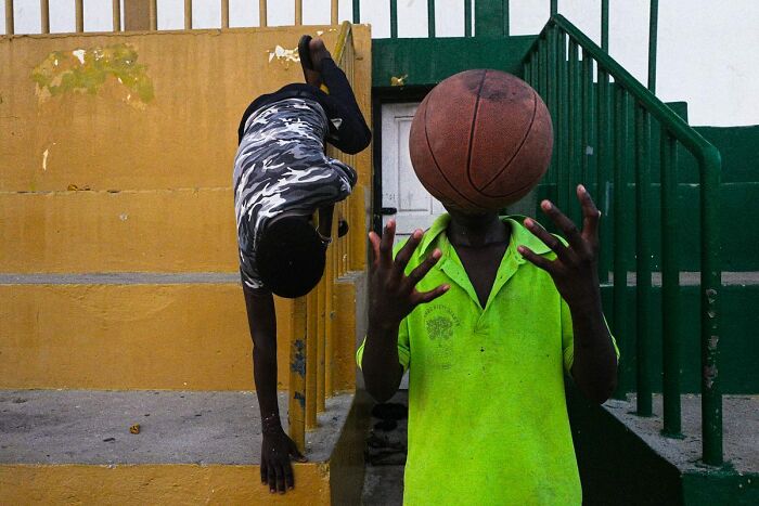 Two people in an urban setting; one performs a handstand while the other balances a basketball, highlighting street photography.