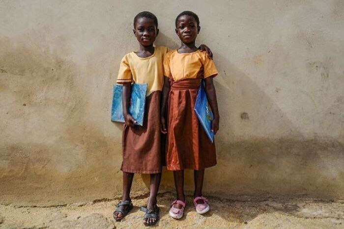 Two children in school uniforms holding books, capturing a moment of everyday life in street photography.