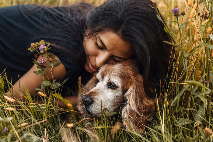 Woman embracing a dog in a field, capturing the special bond between animals and humans, surrounded by wildflowers.