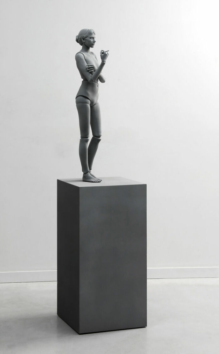 Monochrome sculpture by Hans Op De Beeck depicting a human figure standing on a pedestal in a gallery setting.