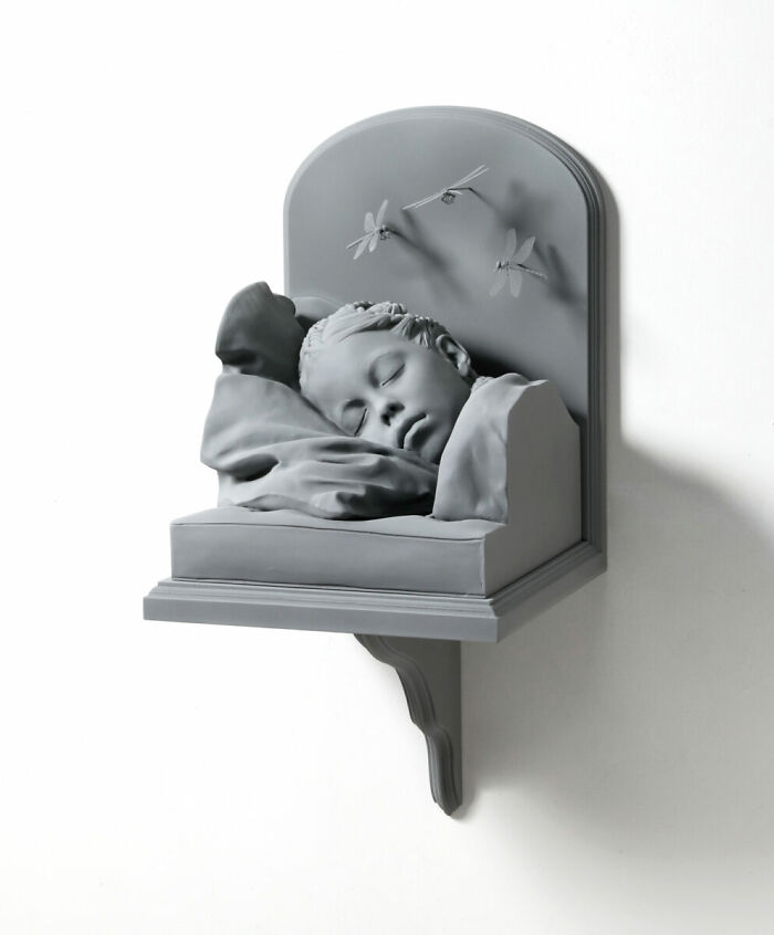 Monochrome sculpture by Hans Op De Beeck of a sleeping child with dragonflies, showcasing serene stillness.