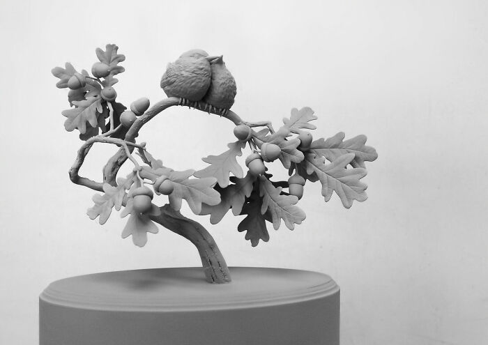 Monochrome sculpture of a bird on a branch by Hans Op De Beeck, featuring detailed leaves and acorns.
