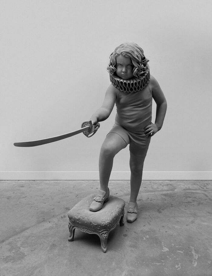 Monochrome sculpture by Hans Op De Beeck depicting a child with a sword on a small ornate stool.