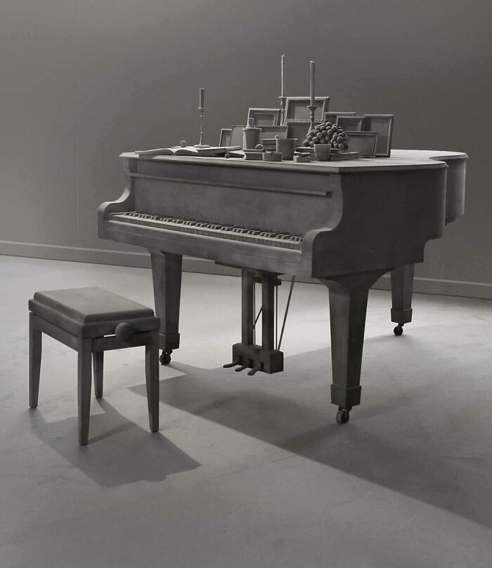 Monochrome sculpture of a piano and bench, adorned with still life objects, by Hans Op De Beeck.