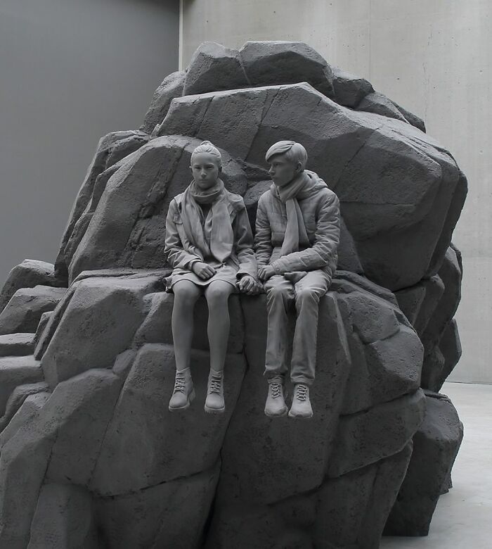 Monochrome sculptures by Hans Op De Beeck: a seated couple on rocky terrain, captured in haunting stillness.
