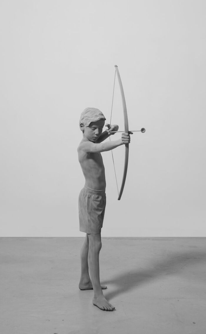 Monochrome sculpture of a boy with a bow, by Hans Op De Beeck, creating a hauntingly still scene.