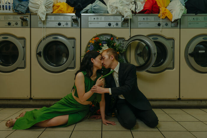Couple in a laundromat, sharing a kiss with floral backdrop, featured in top 2025 engagement photos.