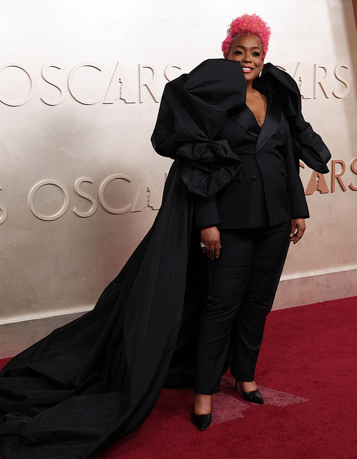 Person on Oscars red carpet in a bold black outfit with pink hair, showcasing a fashionably challenged look from 2025.