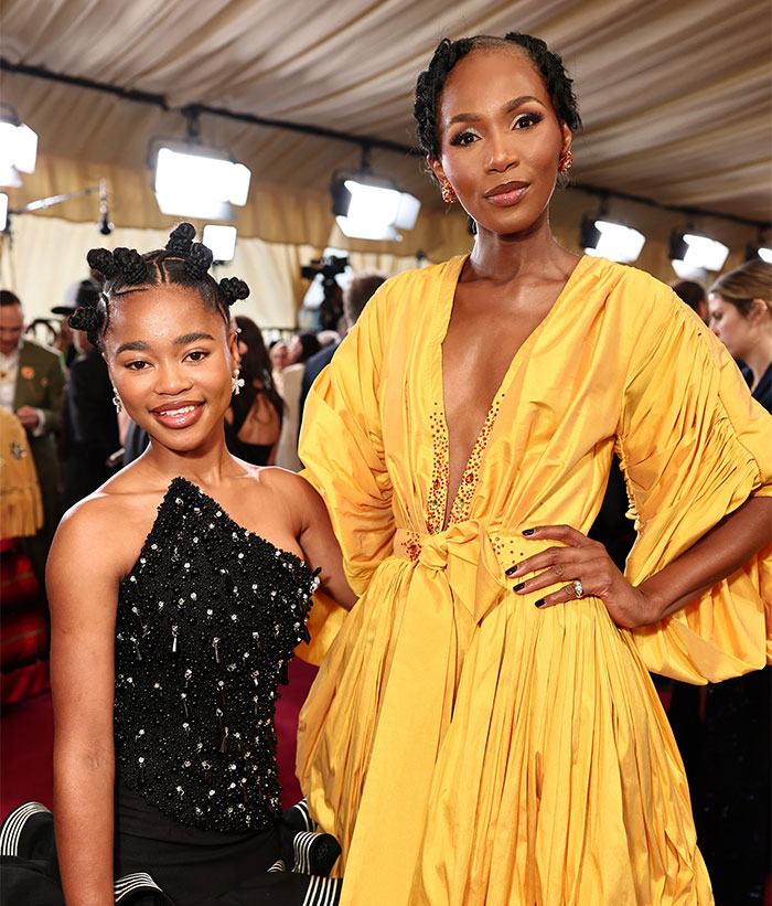 Two women in glamorous dresses at the Oscars 2025, smiling on the red carpet under bright lights.