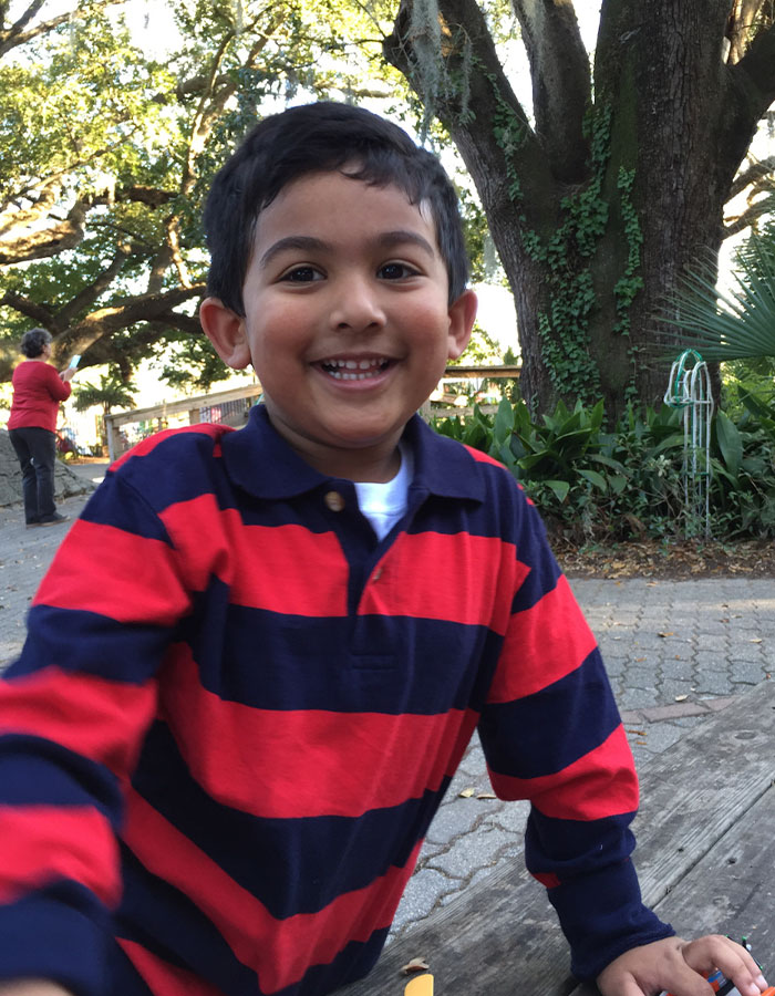 Young boy smiling outdoors, wearing a red and navy striped shirt. Young boy smiling outdoors, wearing a red and navy striped shirt.