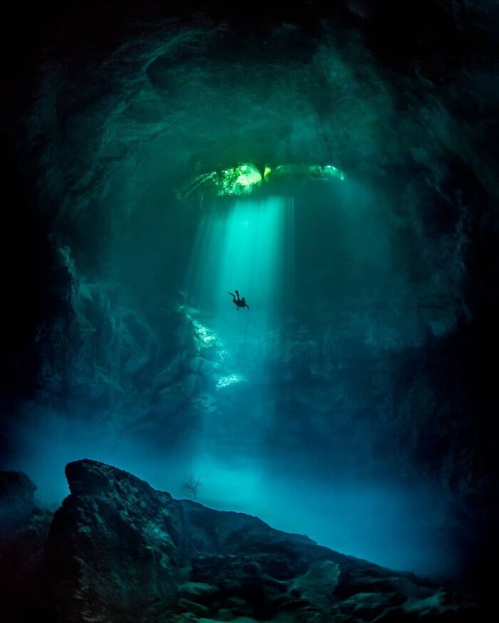 Diver explores an awe-inspiring underwater cave with beams of light streaming through, highlighting iconic natural beauty.