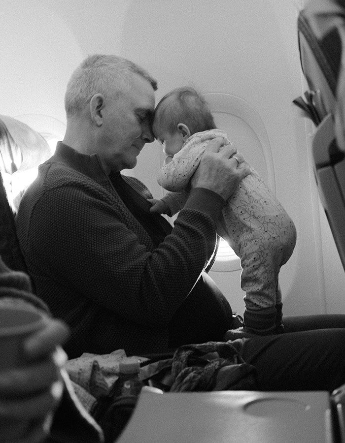 A man and a child on an airplane seat, engaging closely, illuminated by light from a window. A man and a child on an airplane seat, engaging closely, illuminated by light from a window.