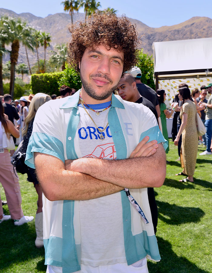 Man with curly hair in a casual outdoor event, wearing a green and white shirt, arms crossed, looking at the camera.