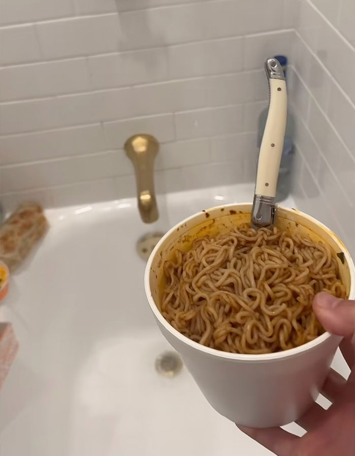 Cup of instant noodles with a knife handle, over a white bathtub, referencing Benny Blanco's shower habit.