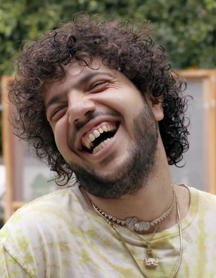 Person with curly hair and necklace, smiling broadly outdoors; topic on shower habit raises fan reactions.
