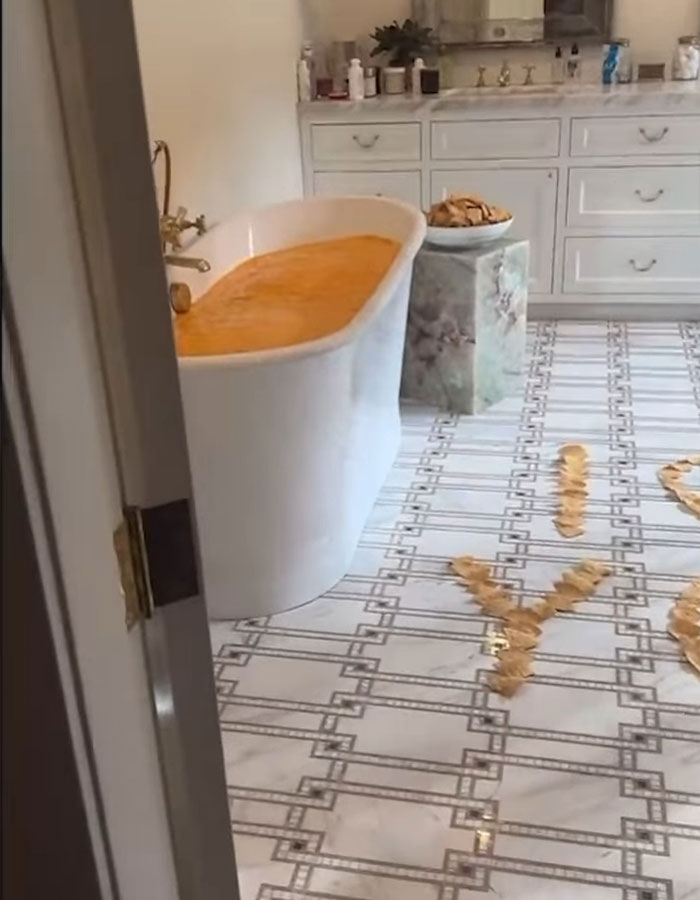 Bathtub filled with an orange liquid, snacks on a stand, and chips arranged on floor&mdash;scene linked to Benny Blanco's shower habit.