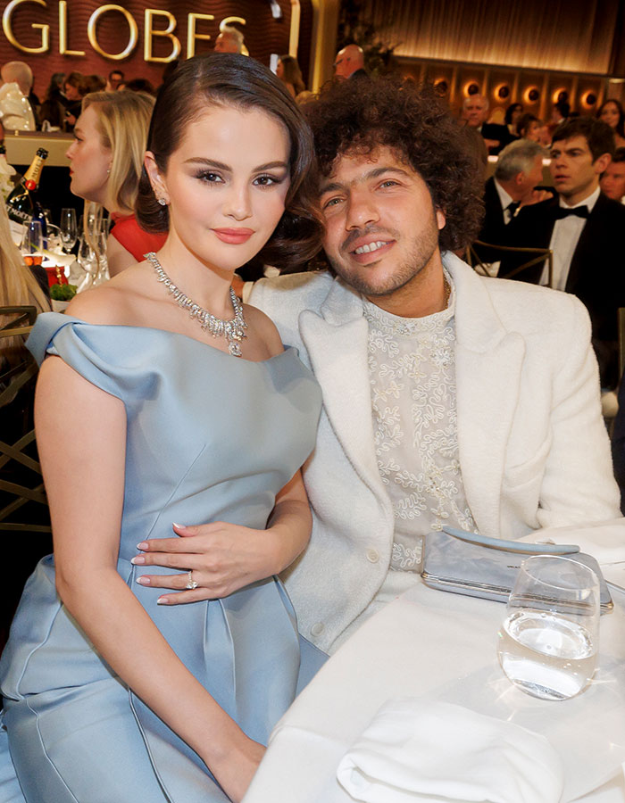 Two attendees dressed elegantly at a formal event table, with glasses and bottles in the background.
