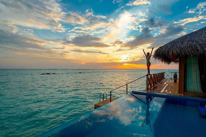 Luxury villa vacation with sunset view over an infinity pool by the ocean, person enjoying serene moment.
