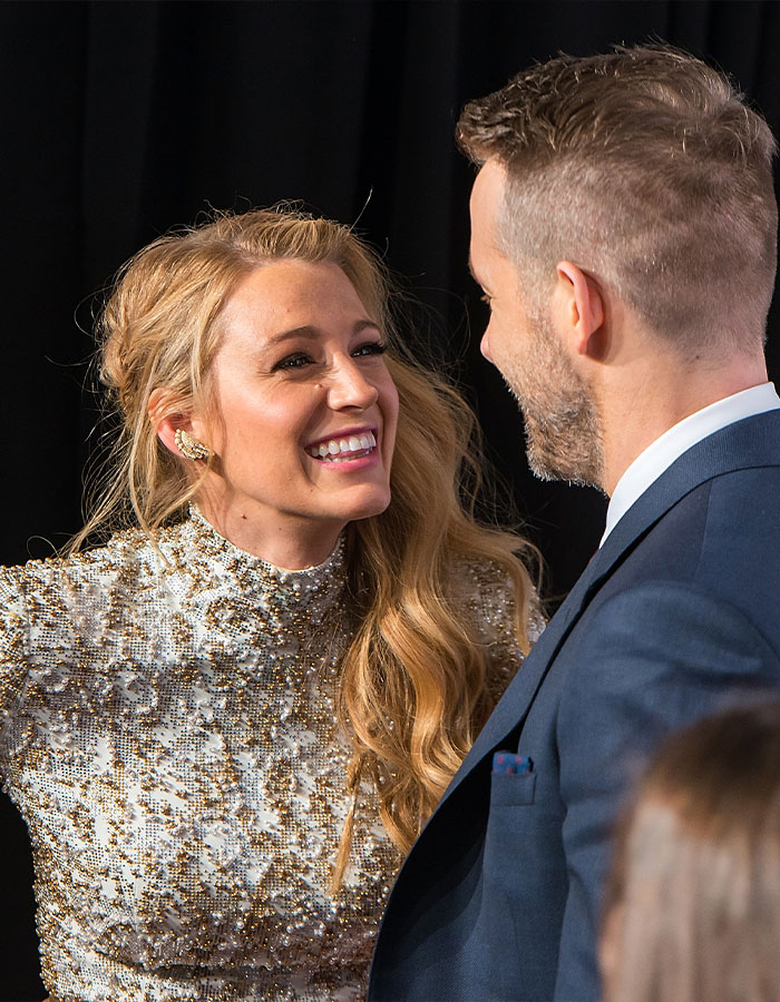 Blake Lively smiling in a sparkling dress on the red carpet, talking to a man in a suit, creating buzz.