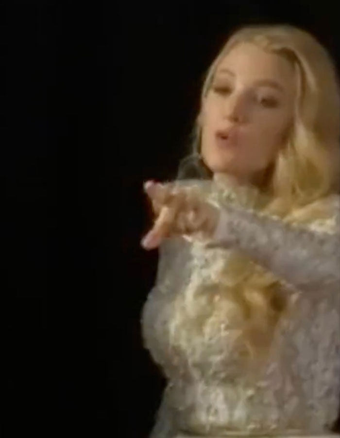 Blake Lively in a white lace dress, gesturing on the red carpet, sparking buzz.