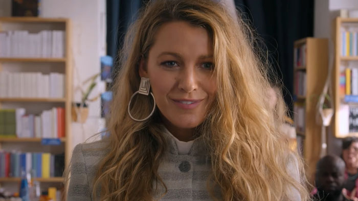 Blonde woman with long hair and large earrings at event, standing in front of bookshelves, related to Team Baldoni. Blonde woman with long hair and large earrings at event, standing in front of bookshelves, related to Team Baldoni.