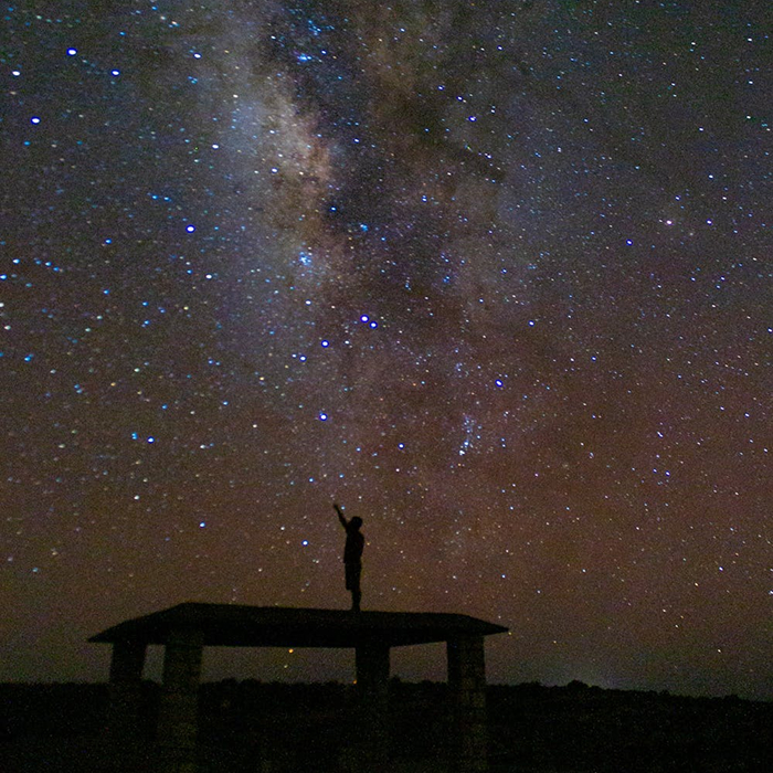 Silhouette of a person stargazing under a starry sky, pointing at the Milky Way, a captivating way to entertain yourself.