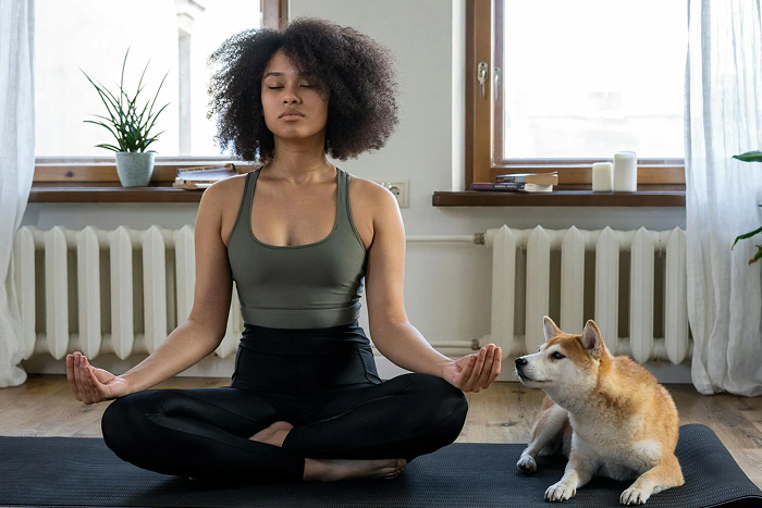 Woman meditating with a dog on a yoga mat, exploring ways to entertain and relax at home.