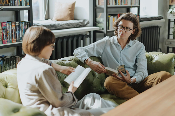 Two people on a green sofa entertaining themselves by reading books in a cozy room with bookshelves.
