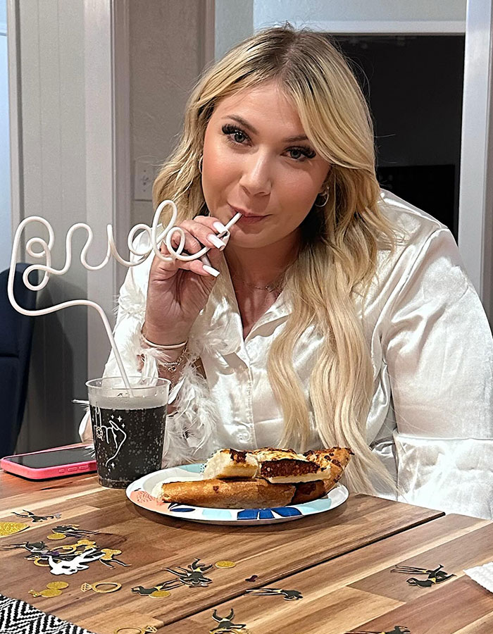 Bride-to-be enjoying pizza and drink with a straw labeled "bride" at a festive bachelorette party.