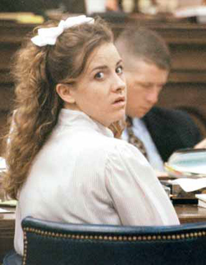 Woman at a courtroom table with an overturned conviction, wearing a bow in her hair and a white shirt.