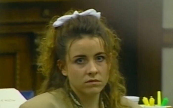 Woman with conviction overturned, wearing a white hair bow, looking serious in a courtroom setting.