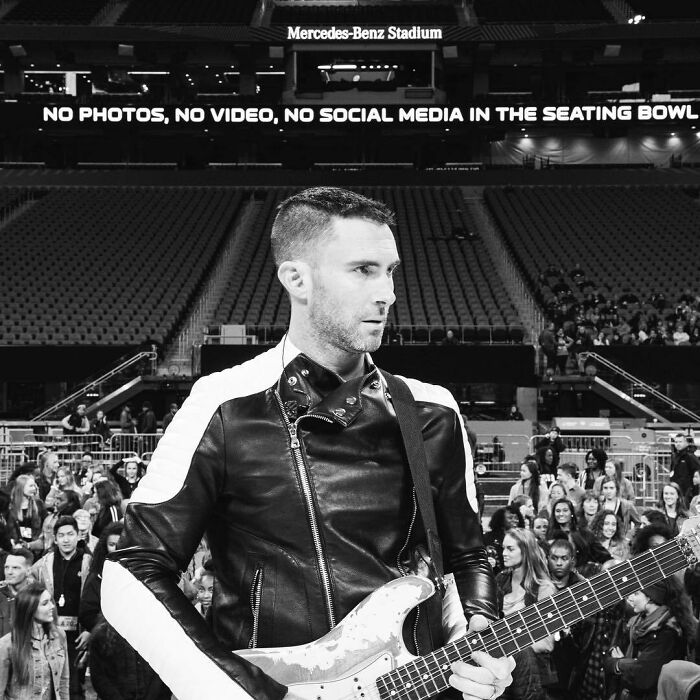 Musician in a leather jacket holding a guitar at Mercedes-Benz Stadium, controversial attractiveness.