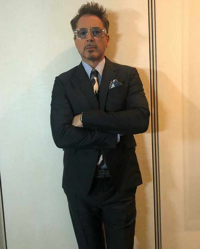 Man in a suit with glasses, arms crossed, against a wall, representing not-self-made-celebs theme.