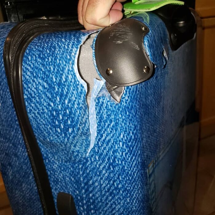 Damaged airline baggage with torn blue suitcase fabric and broken handle.
