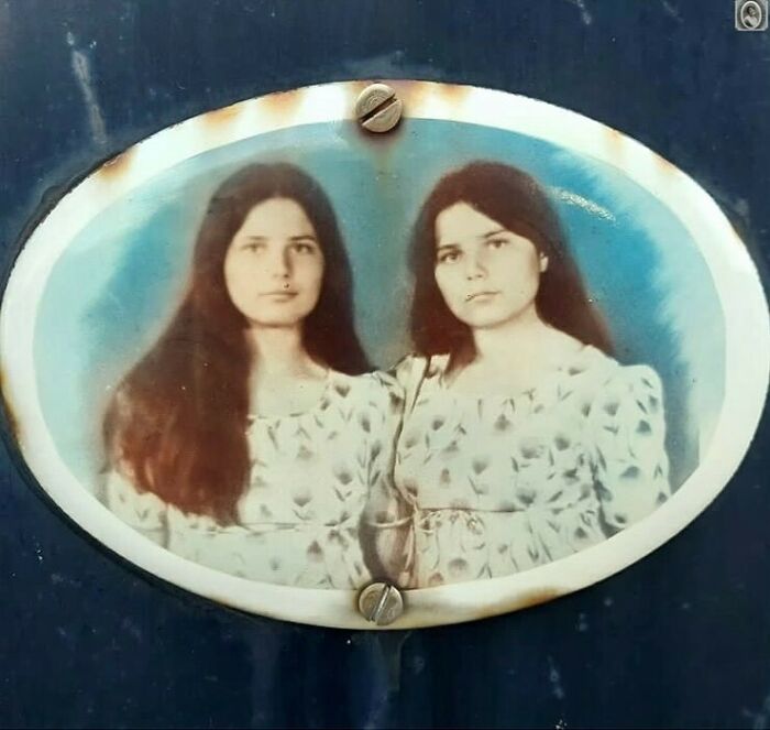 Two women with long hair on a lovely headstone portrait, both wearing patterned dresses against a blue background.