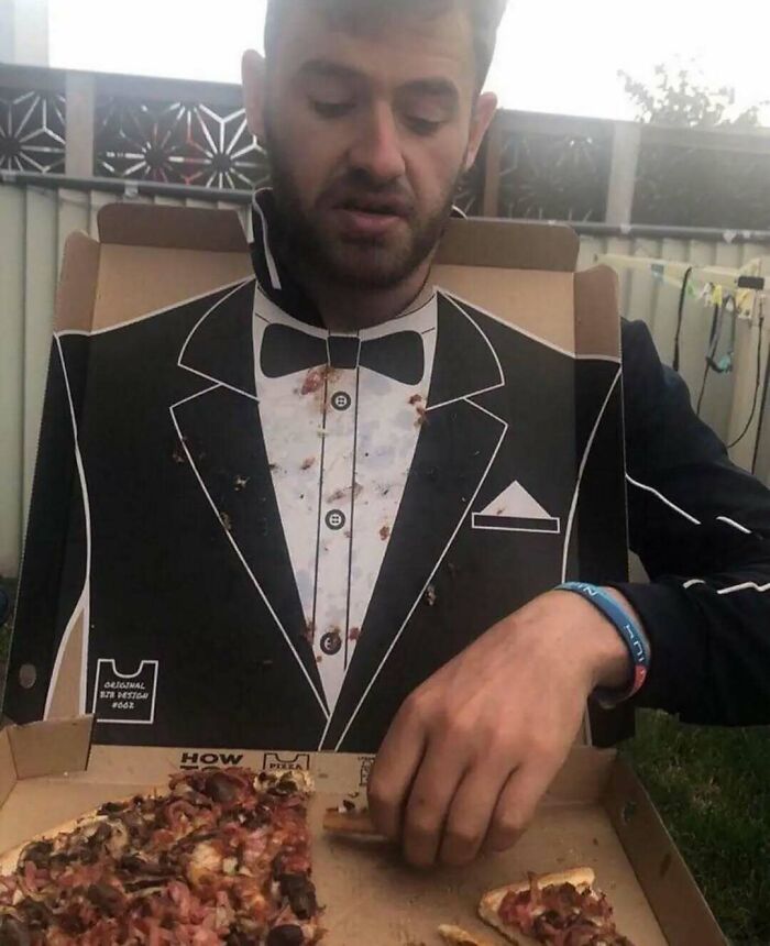 Man eating pizza wearing a tuxedo print t-shirt, showcasing chaotic humor.