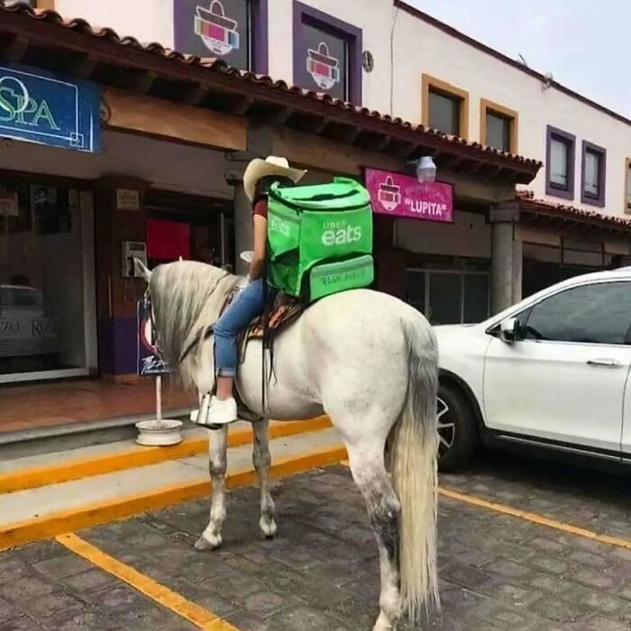 Repartidor de comida sobre caballo frente a tienda, mochilera verde destaca tema de comida caótica.