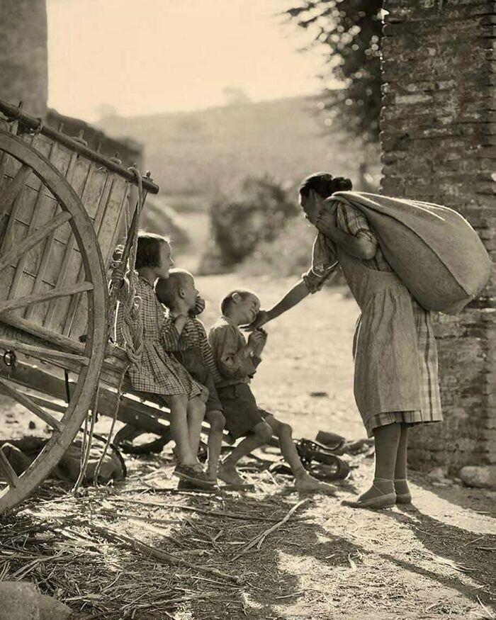 Woman and three children by a cart in a historical setting, evoking nostalgia.