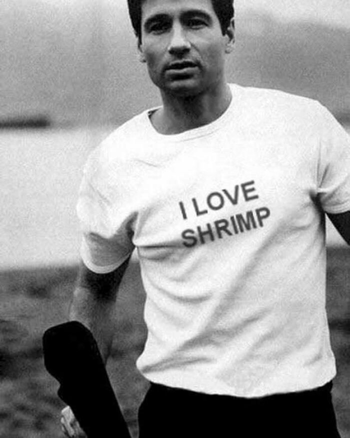 Man wearing chaotic T-shirt with "I Love Shrimp" text, standing outdoors.