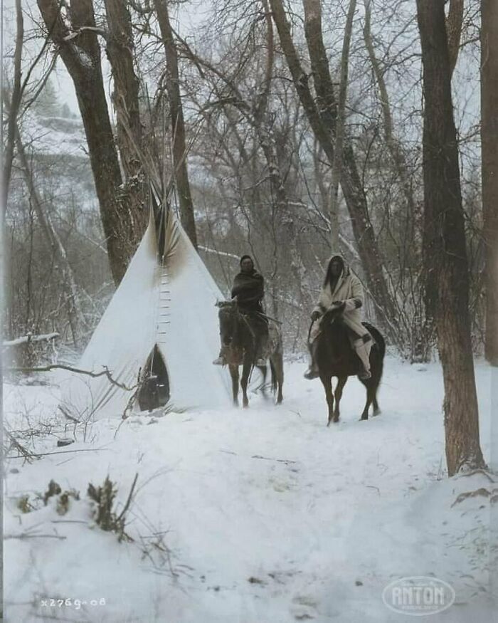Historical image of two people on horseback in snowy forest near a tipi.